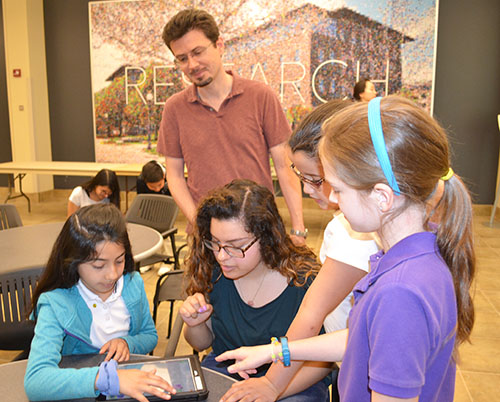 Yann Chemla (center back) watches Lina Flores teach IPA students how to program their Dash robot.