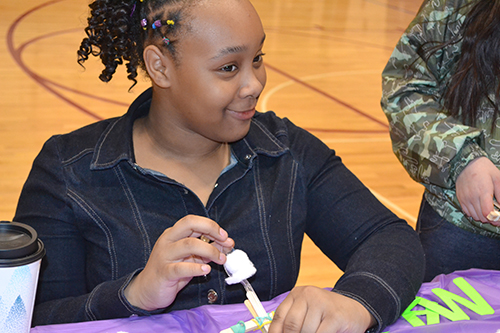 A STEAM Night visitor prepares to lob a cotton ball at the target: a plastic cup pyramid.