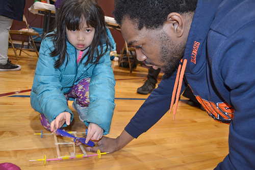 Kingsley Okeke (right), helps a young visitor test her rubberband helicopter.