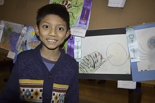 A young visitor proudly poses with the drawing he made as part of the art contest