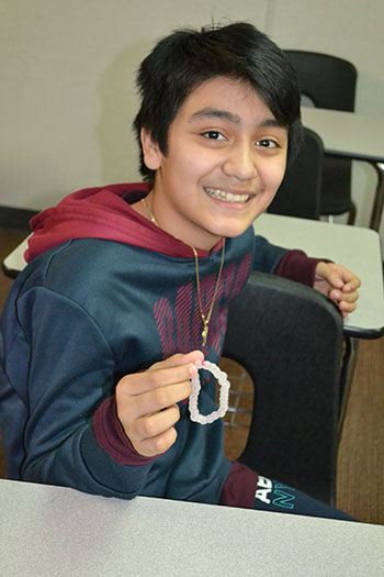 A seventh grade boy proudly displays the bracelet he made.