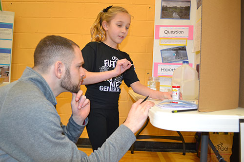 Scott Blanck, a teacher at Next Generation School's STEAM Studio after-school program watches a student do a ph test as part of her presentation at the Science and Engineering Fair.