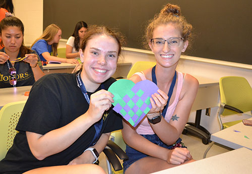 Two freshmen show off the 3D paper heart they made.