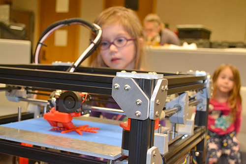 A young participant watches as a 3D printer manufactures a starfish.