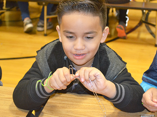 A young Cena y Ciencias visitor works on putting together their paper clip chain.