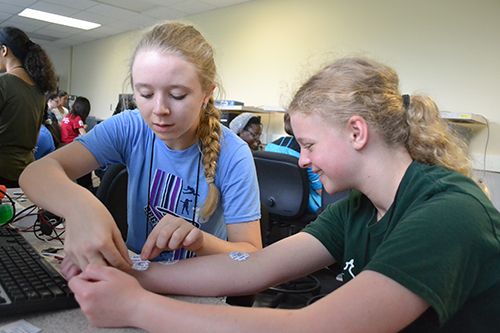 A BioE GAMES participant places sensors on another student's arms during the muscle strength activity.