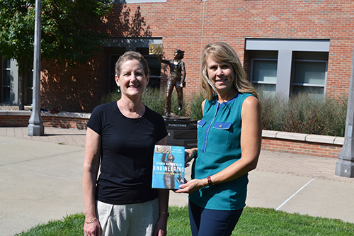 Laura Hahn (left) and Angie Wolters (right) with their book in front of the Quintessential Engineer statue.