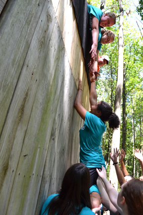 WIE camper climbs the tall wall with the help of her teammates.